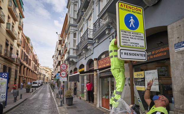 Dos operarios de Movilidad colocan una señal en la que se informa de la prioridad peatonal de SanAntón. 