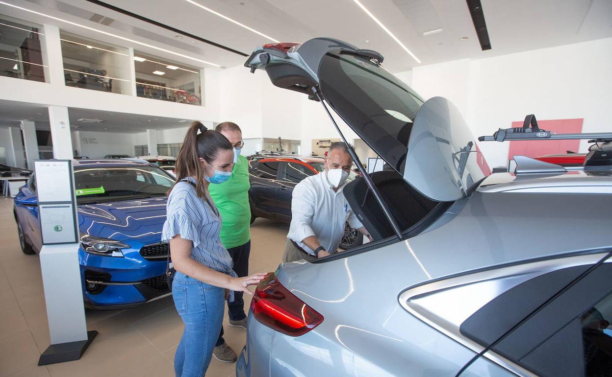 Un vendedor enseña el maletero de un vehículo en un concesionario a unos posibles compradores. 