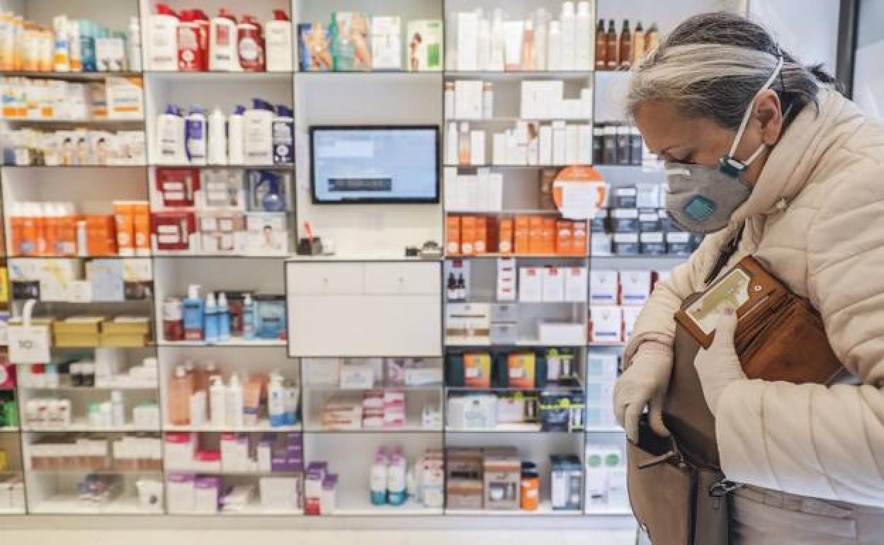 Una mujer, protegida con mascarilla, entra en una farmacia. 