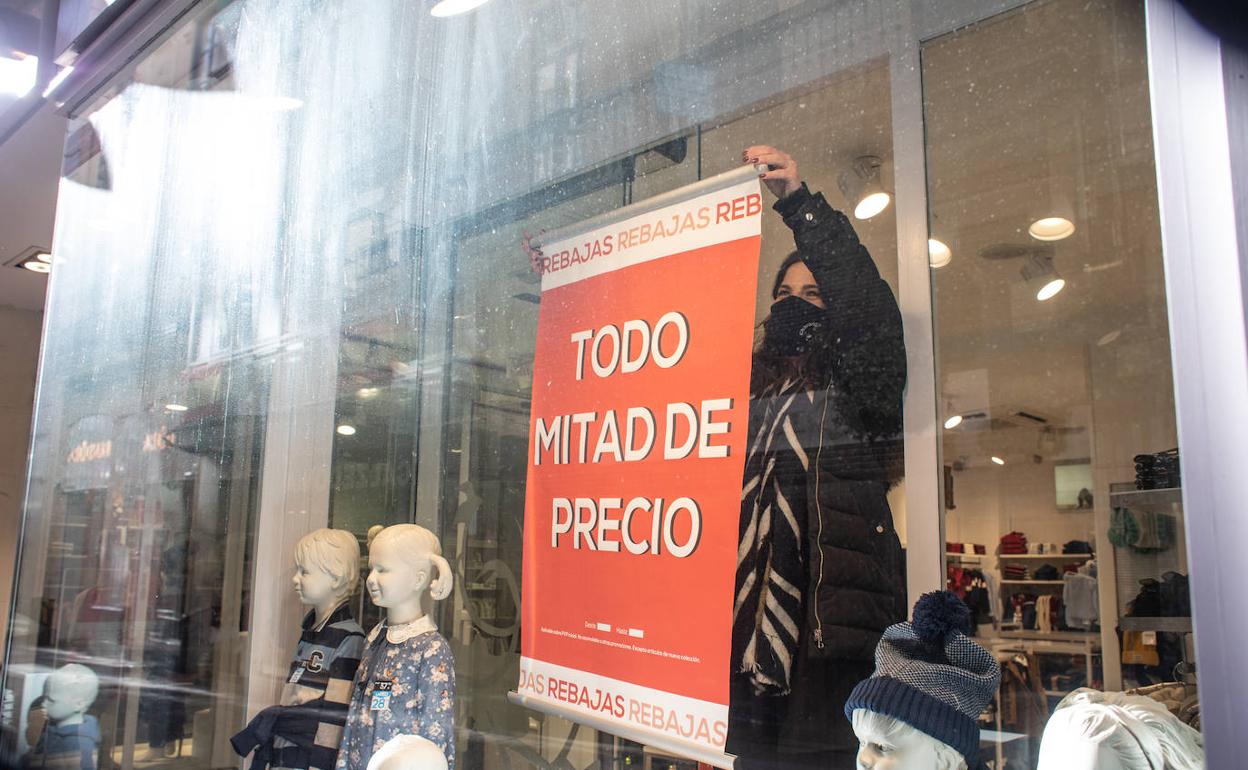 Una dependienta de un comercio del Centro coloca un cartel de rebajas en el escaparate.