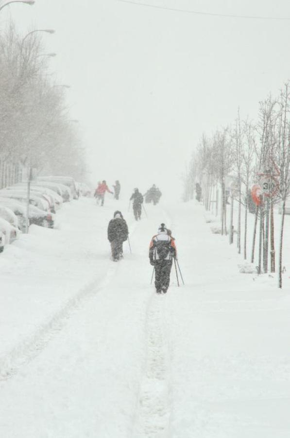 Algunas personas caminan por una calzada completamente cubierta de nieve de una calle en Alcobendas, Madrid