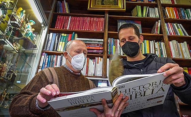 El librero hojea con su hijo Javier, que le ha relevado al frente del negocio, uno de los títulos que se pueden adquirir en su establecimiento. 