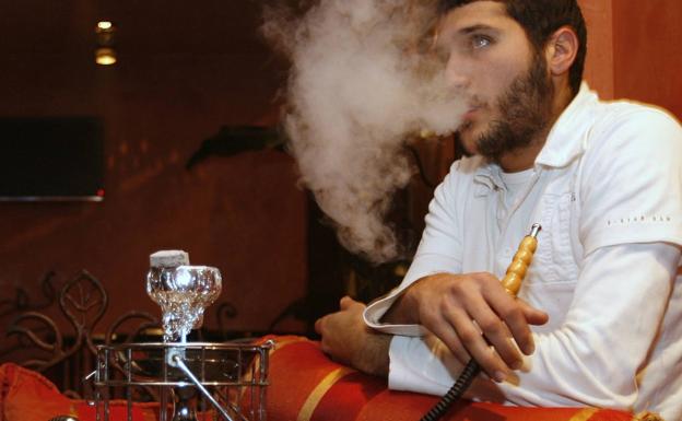 Un joven fuma tabaco con una cachimba en un café de París.