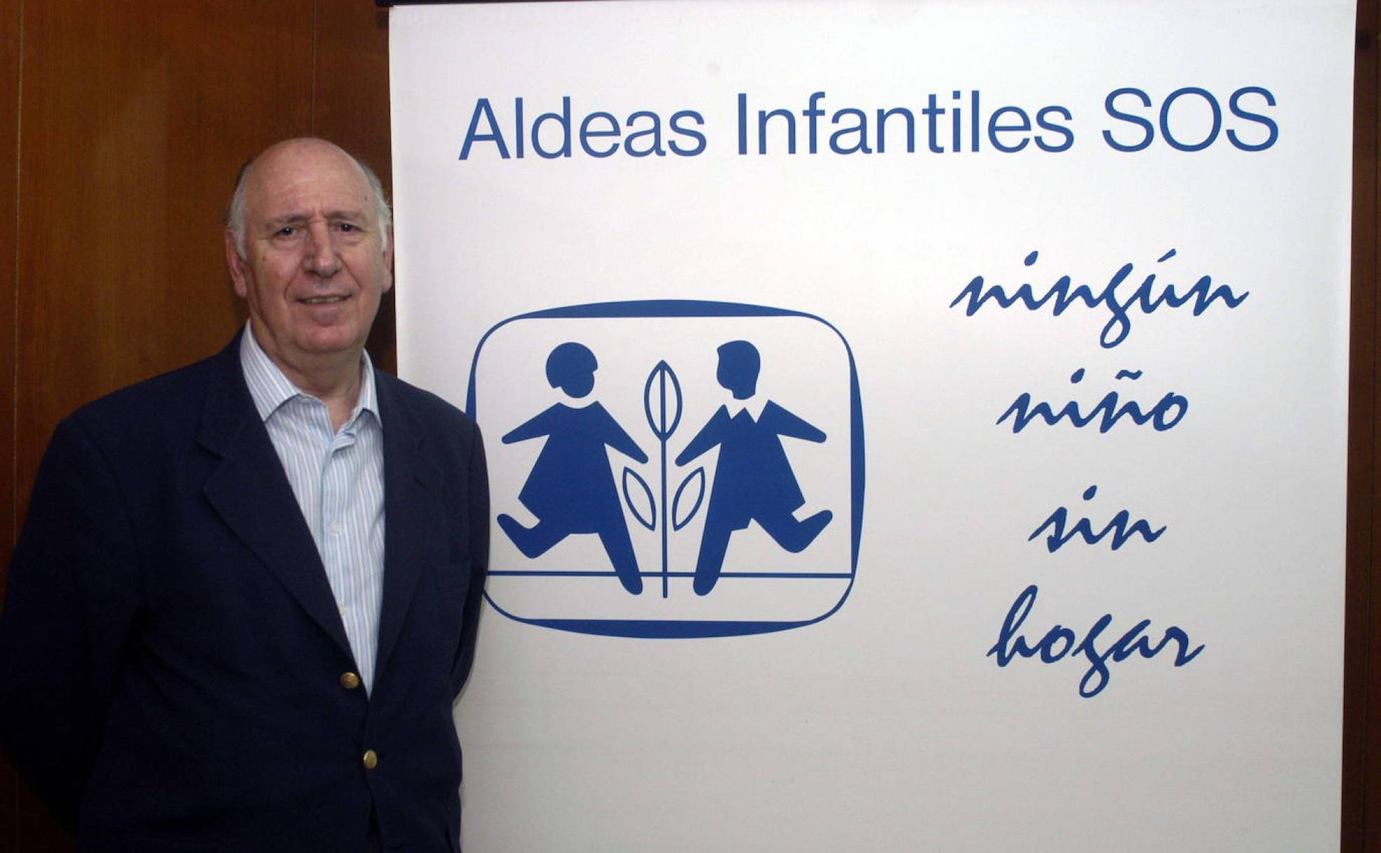 Junto a un cartel de la organización que preside como fundador en España.