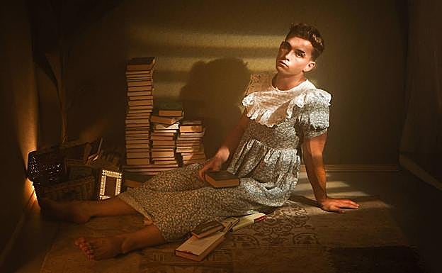 Chico vestido de chica en una habitación con libros, una de las ensoñaciones incluida en la exposición. 