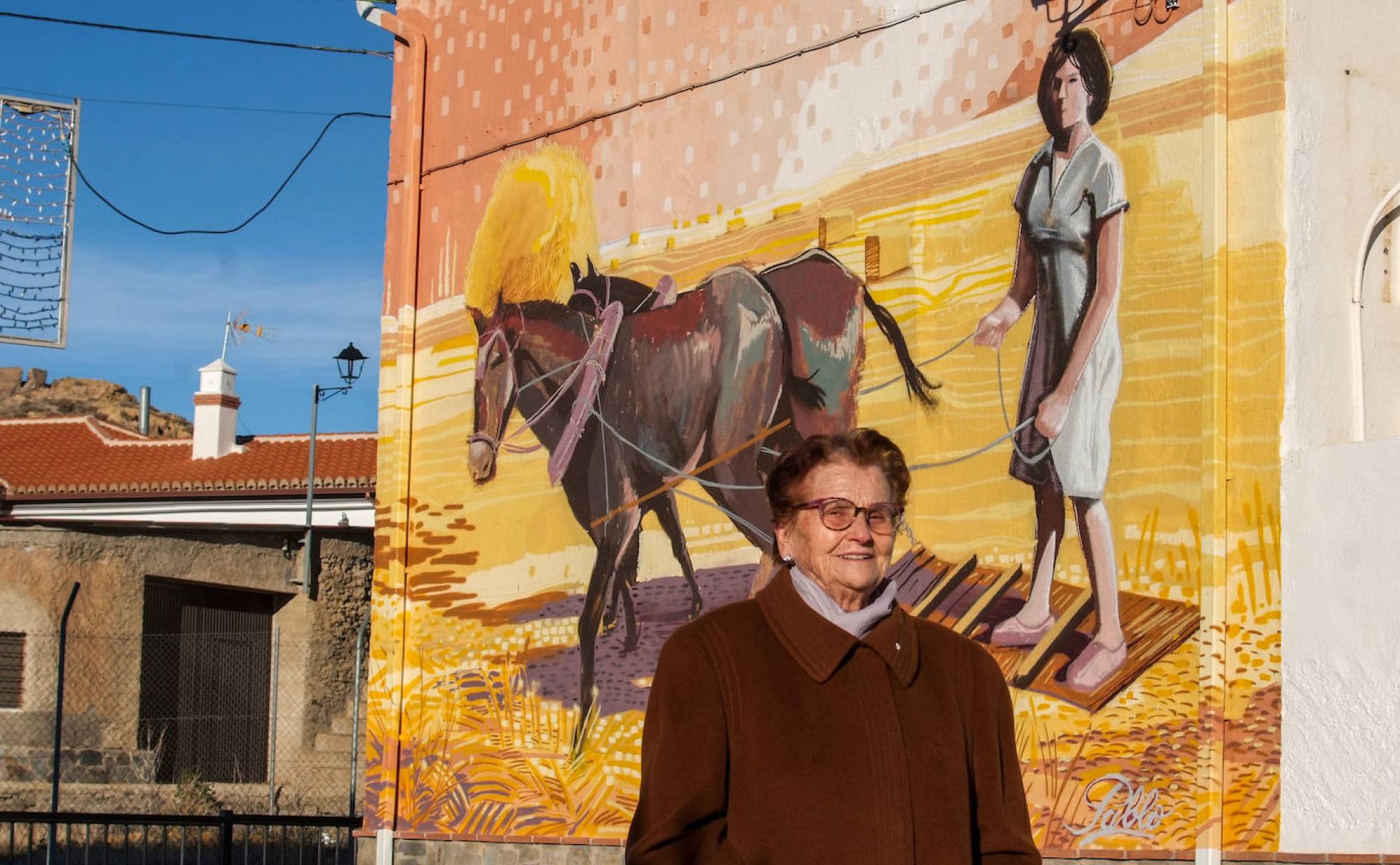 Encarna, de 91 años, sentada bajo un grafiti dedicado a la trilla, en Dólar. 