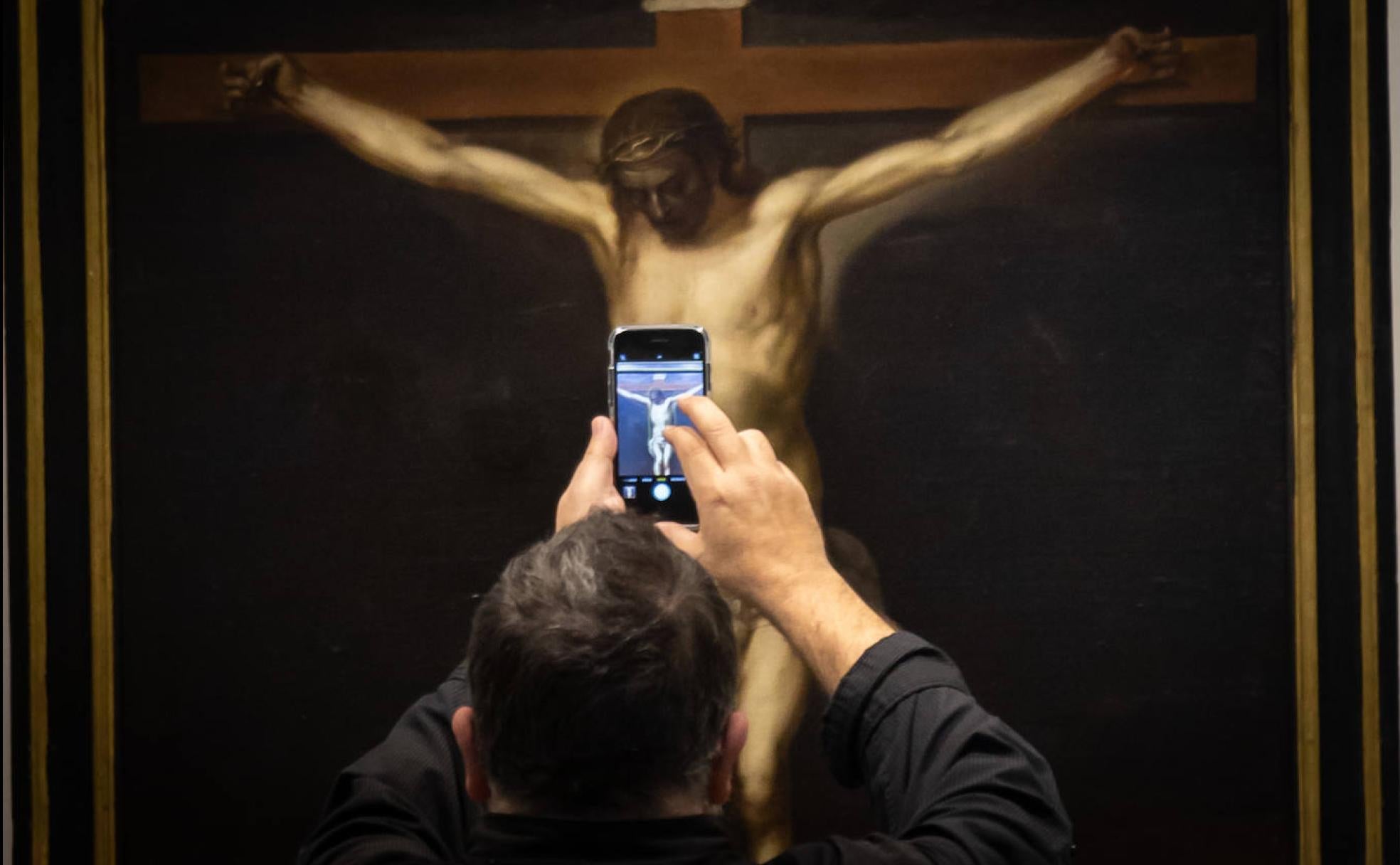 Un hombre fotografía con su móvil el Cristo de Alonso Cano expuesto en Gran Capitán. 