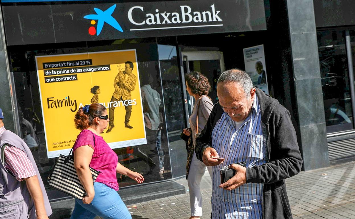 Un hombre guarda dinero ante una oficina de CaixaBank en Barcelona. 