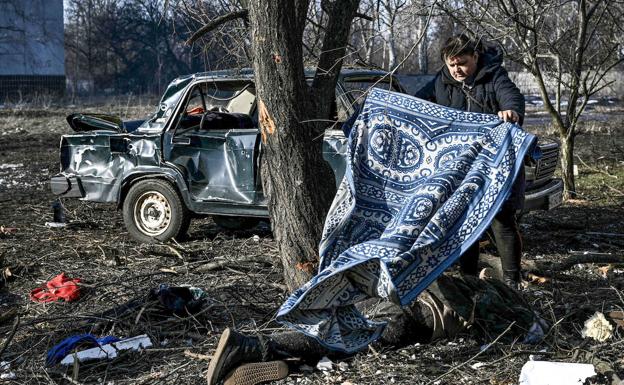 Imagen principal - Arroba. Primeros fallecidos. Un vecino de Chuguev, al este de Ucrania, tapa con una manta a una víctima de los ataques rusos. Debajo. Bombardeos. Un hombre herido en Járkov; y una familia camina a la frontera con Hungría. 