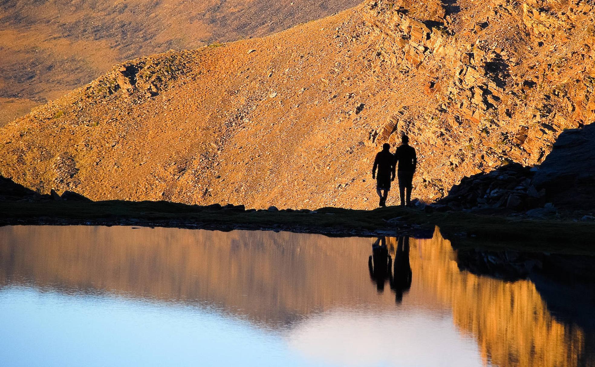 Senderistas reflejados en la Laguna de la Mosca en un atardecer en Sierra Nevada. 