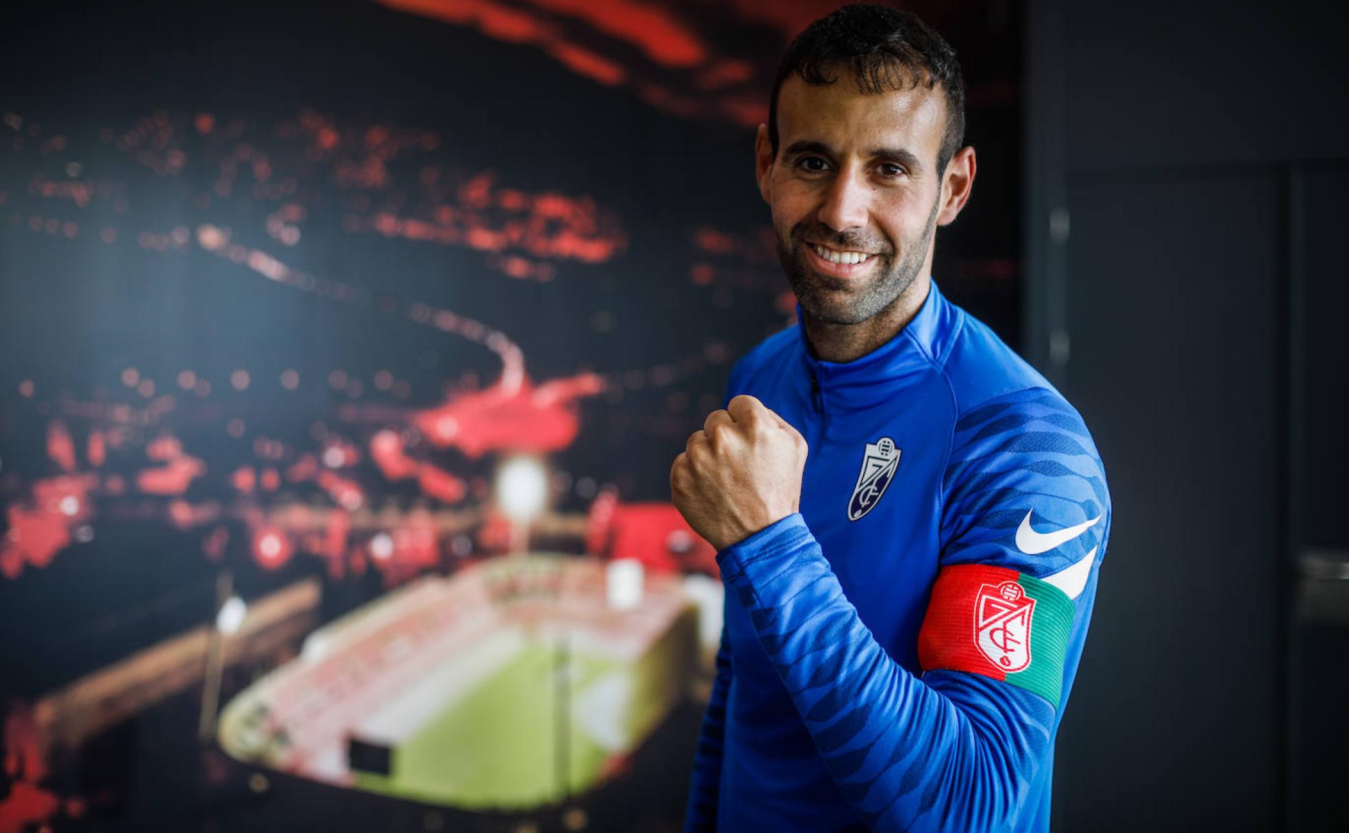 Víctor Díaz porta el brazalete de capitán ante una pared con una ilustración de Los Cármenes en la Ciudad Deportiva del club.