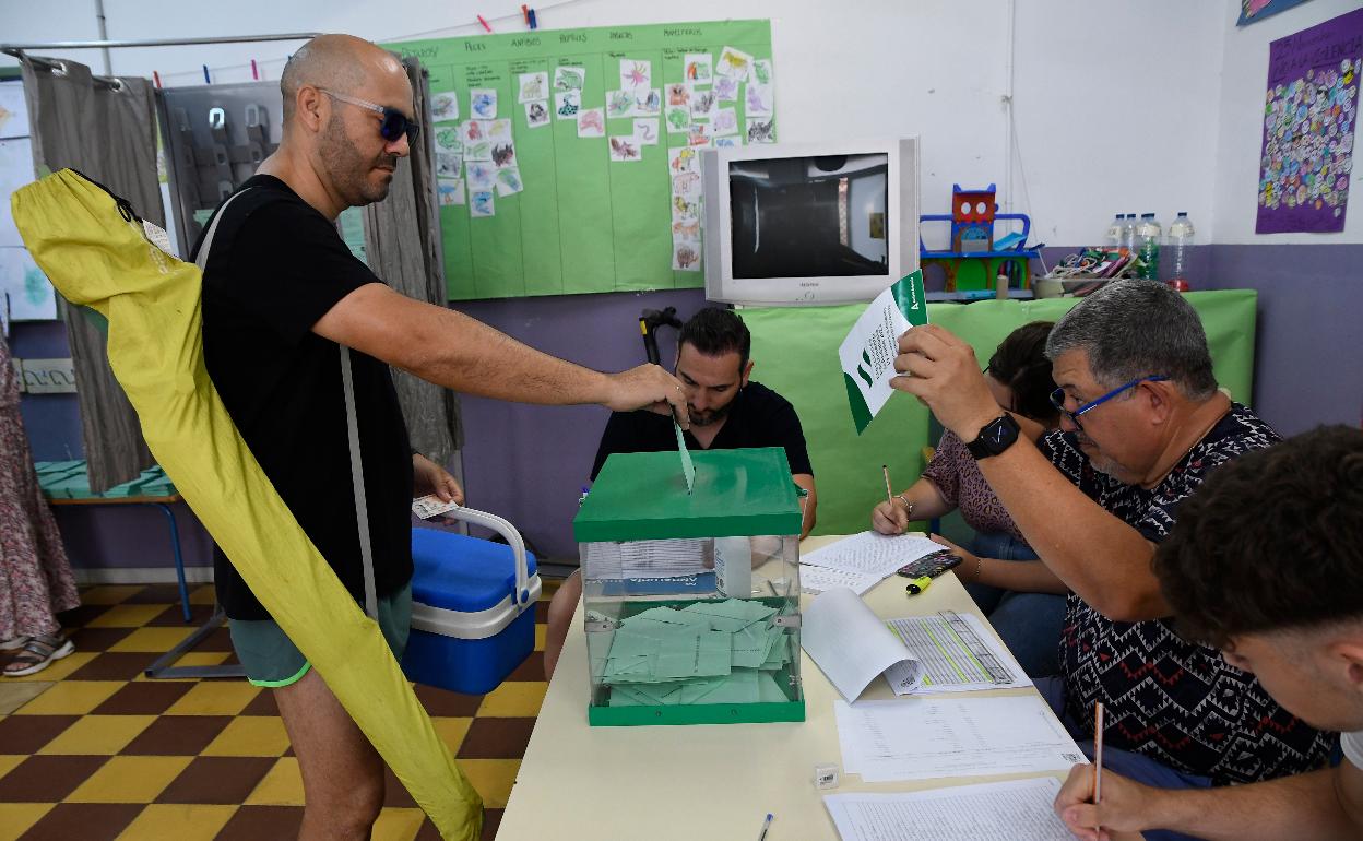 Un hombre con la sombrilla al hombro vota en un colegio electoral de Roquetas de Mar.