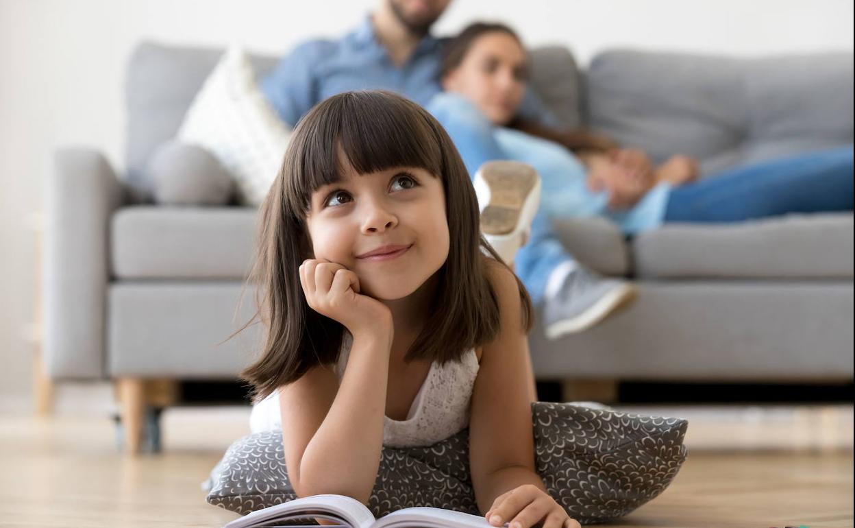 Una niña lee en el suelo e imagina. 