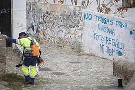 Personal de mantenimiento barre una calle del Albaicín con una pintada que dice 'no tengas prisa, yo te regalo mi tiempo'. .