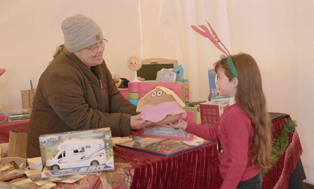 Una pequeña entrega un regalo en la carpa de RB Interiorismo.