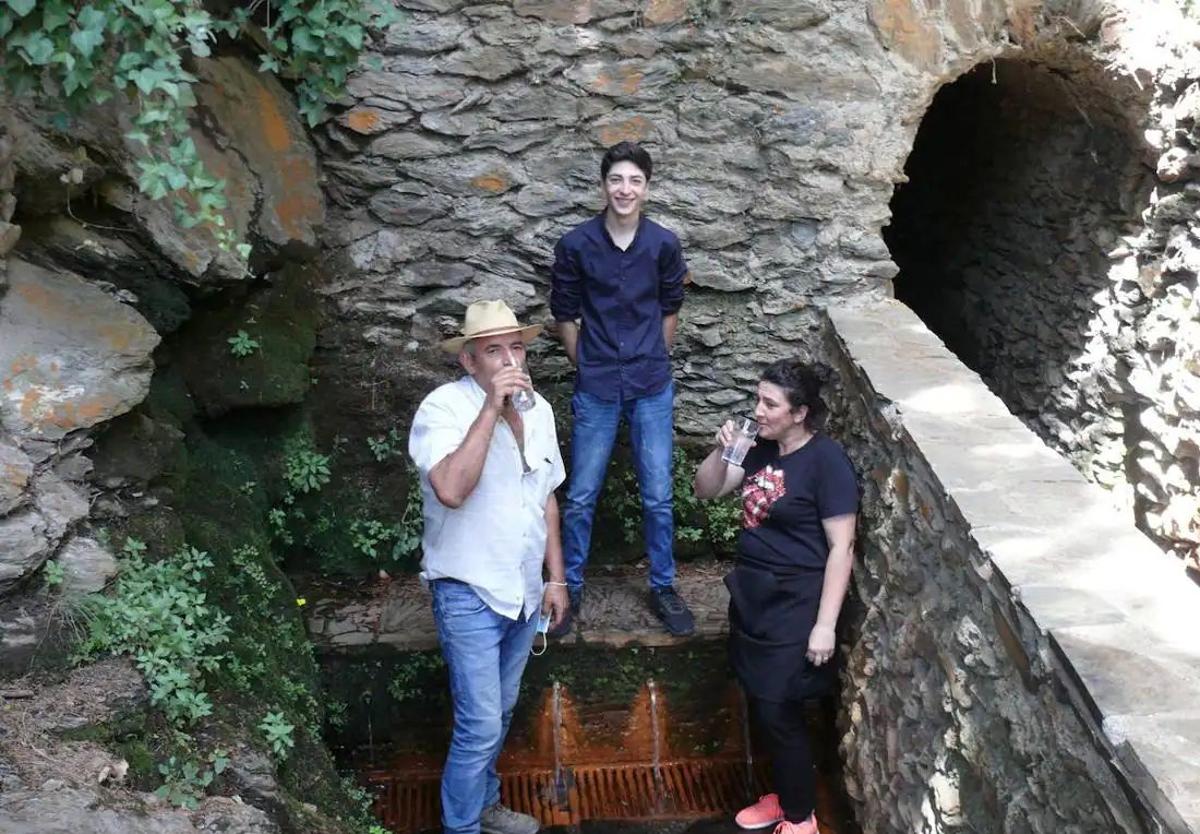 Dos personas beben agua de la Fuente Agria de Pórtugos.