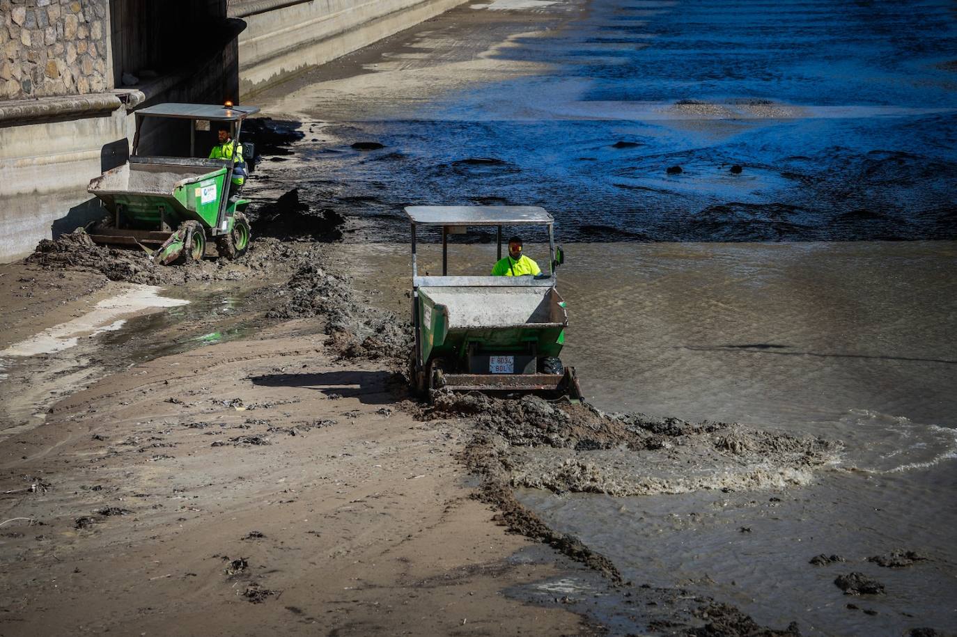 Dos operarios retiran lodo del río Genil a su paso por Granada.