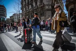 Turistas con sus maletas cruzan el paso de cebra de Gran Vía este sábado-