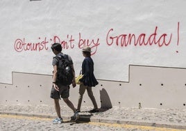 Una pareja pasea por el Albaicín ante una pintada contra la turistificación en el año 2019.