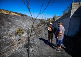 Dos vecinos observan junto a las viviendas el terreno arrasado por las llamas.