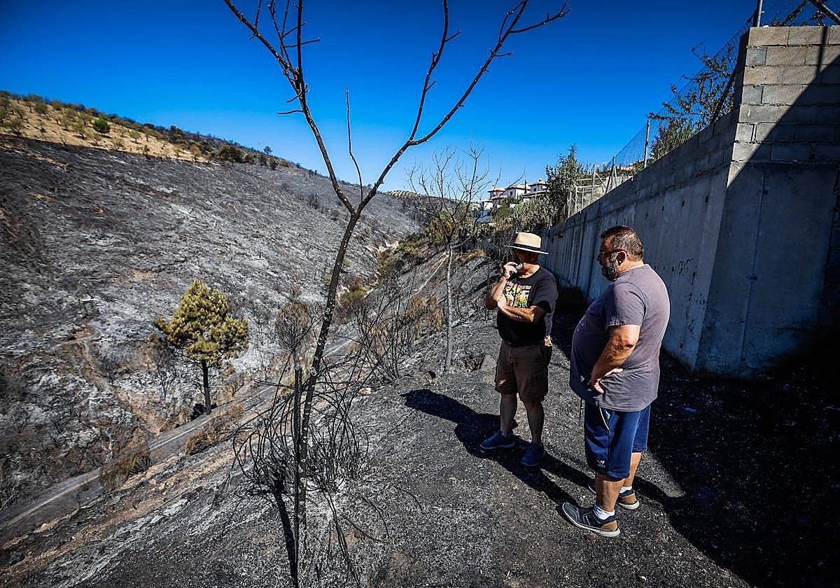 Dos vecinos observan junto a las viviendas el terreno arrasado por las llamas.