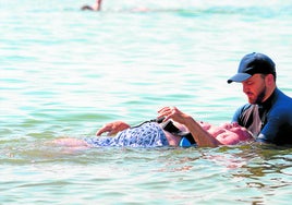 Un anciano se baña en la playa con ayuda de un socorrista.