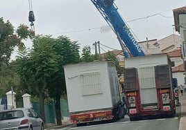 Una grúa inicia la colocación de dos aulas prefabricadas en un centro educativo.