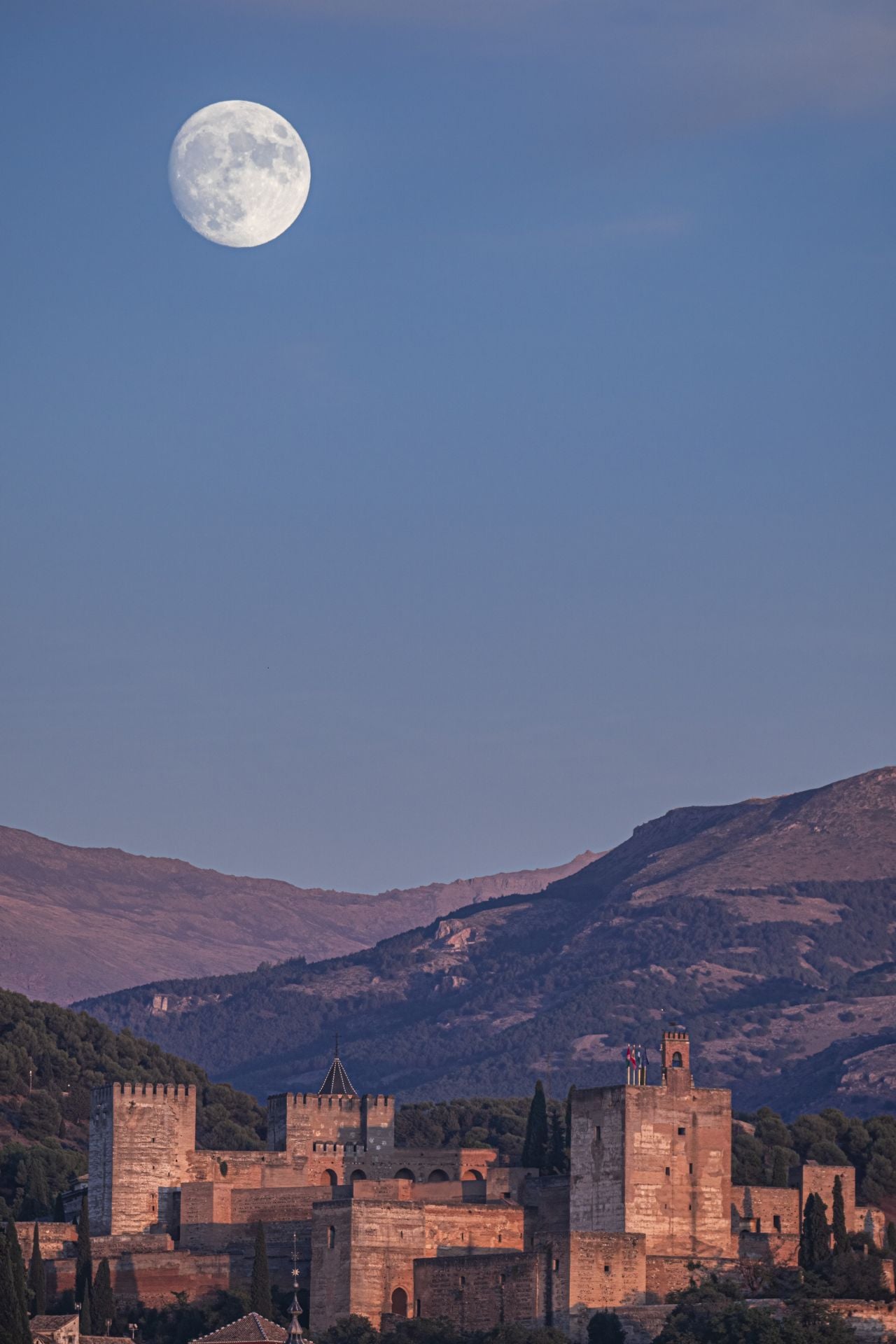 La Luna llena 'alumbrando' el conjunto monumental de la Alhambra a la hora del ocaso.