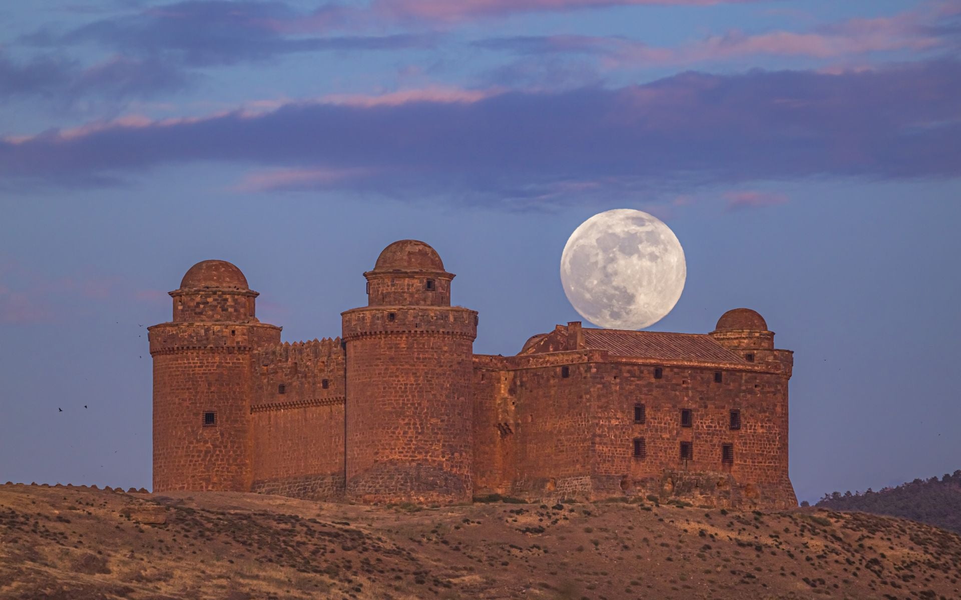 La Luna aflora de uno de los tejados del castillo renacentista de la Calahorra.