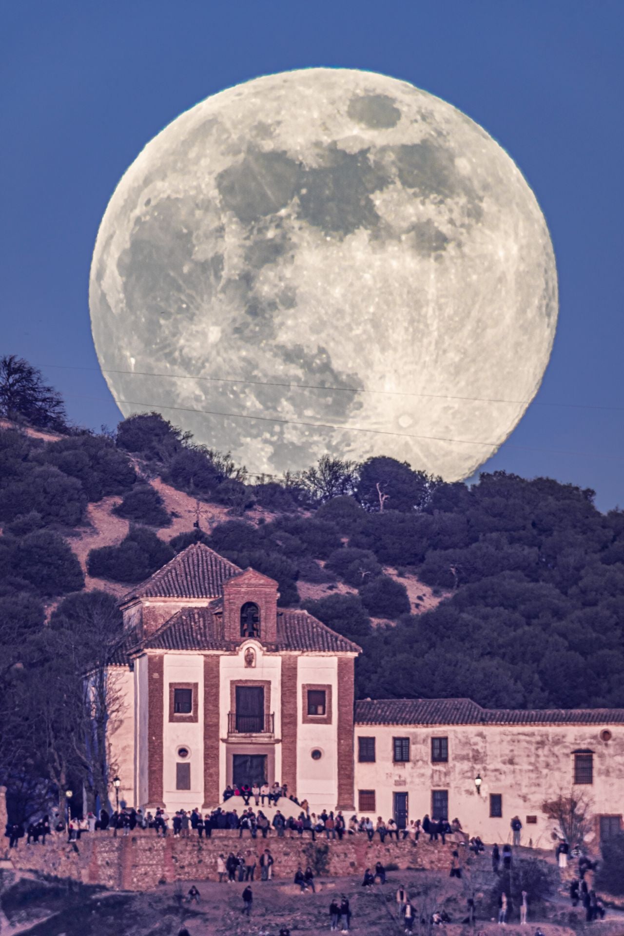 La Luna llena, en la que se identifica toda so geografía, emergiendo por detrás de la pequeña ermita de San Miguel Alto de Granada.