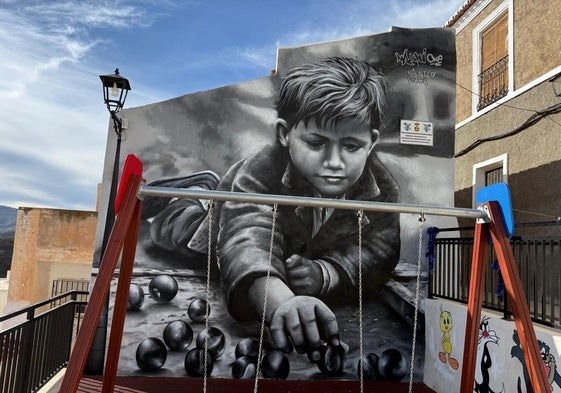 Grafiti de un niño jugando a las canicas en el suelo.