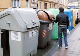 Un vecino tira una bolsa de basura al contenedor marrón durante el día.