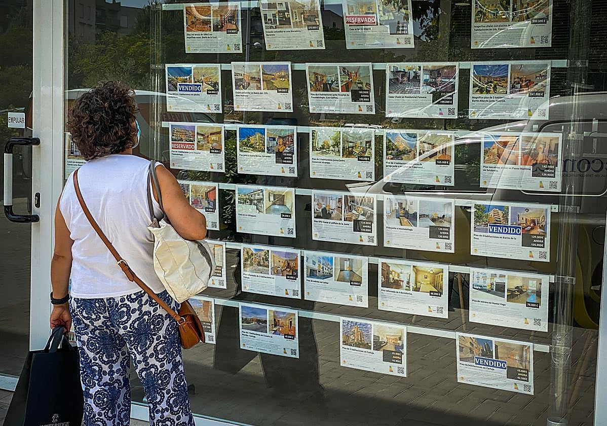 Una mujer consulta ofertas de viviendas en el escaparate de una inmobiliaria.