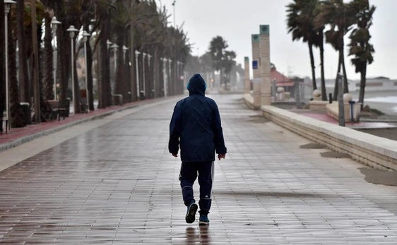Un hombre camina por el Paseo Marítimo bajo un temporal de lluvia y viento.