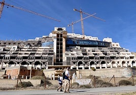 Dos senderistas caminan frente a las obras paralizadas del Hotel El Algarrobico, a apenas unos metros del agua del mar.