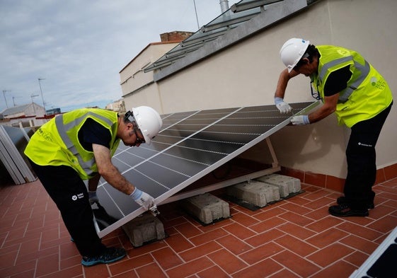 Dos instaladores trabajan en los paneles solares en el tejado de un edificio de viviendas.