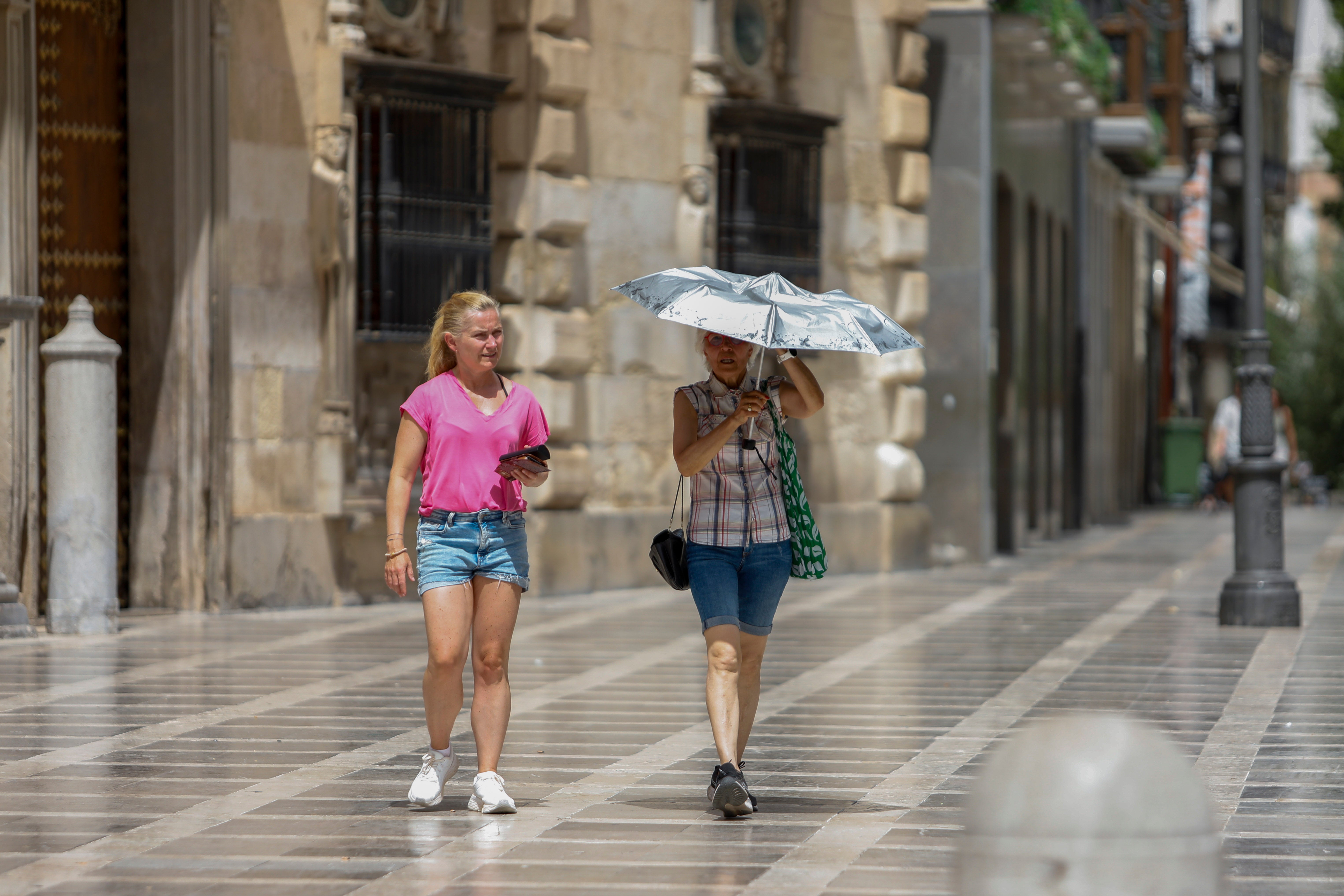 Dos turistas tapándose del sol con un paraguas