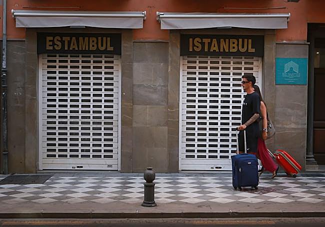 Persianas cerradas y turistas tirando de maletas.