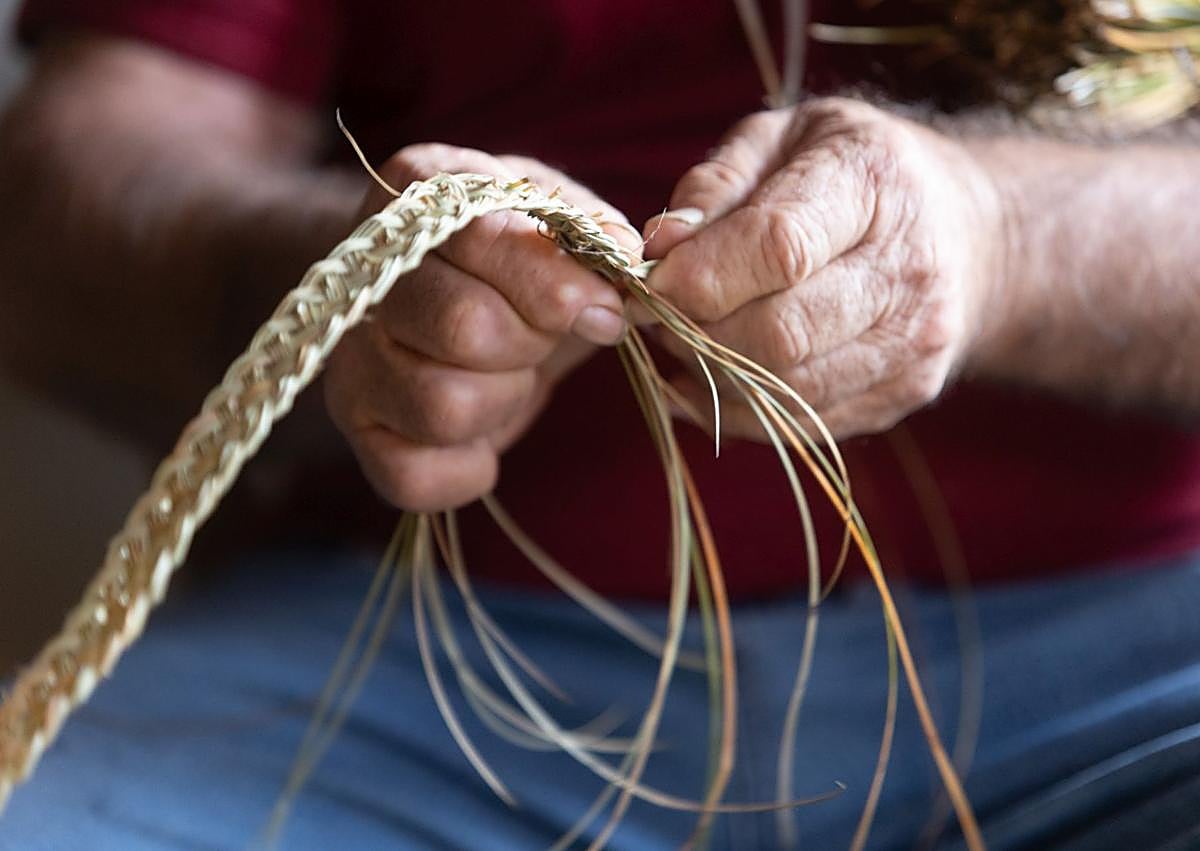 Imagen secundaria 1 - Las manos de Manuel muestran cómo trenzar esparto y arriba una reproducción de la Catedral de Granada con esparto.