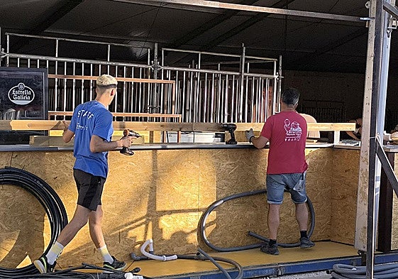 Dos operarios montan una caseta en el recinto ferial.