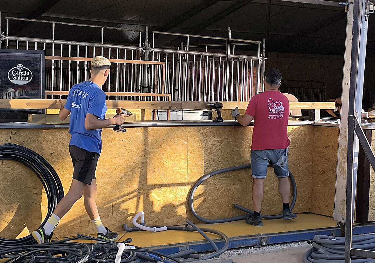 Dos operarios montan una caseta en el recinto ferial.