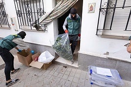 Un agente sale de una casa con una bolsa llena de marihuana.
