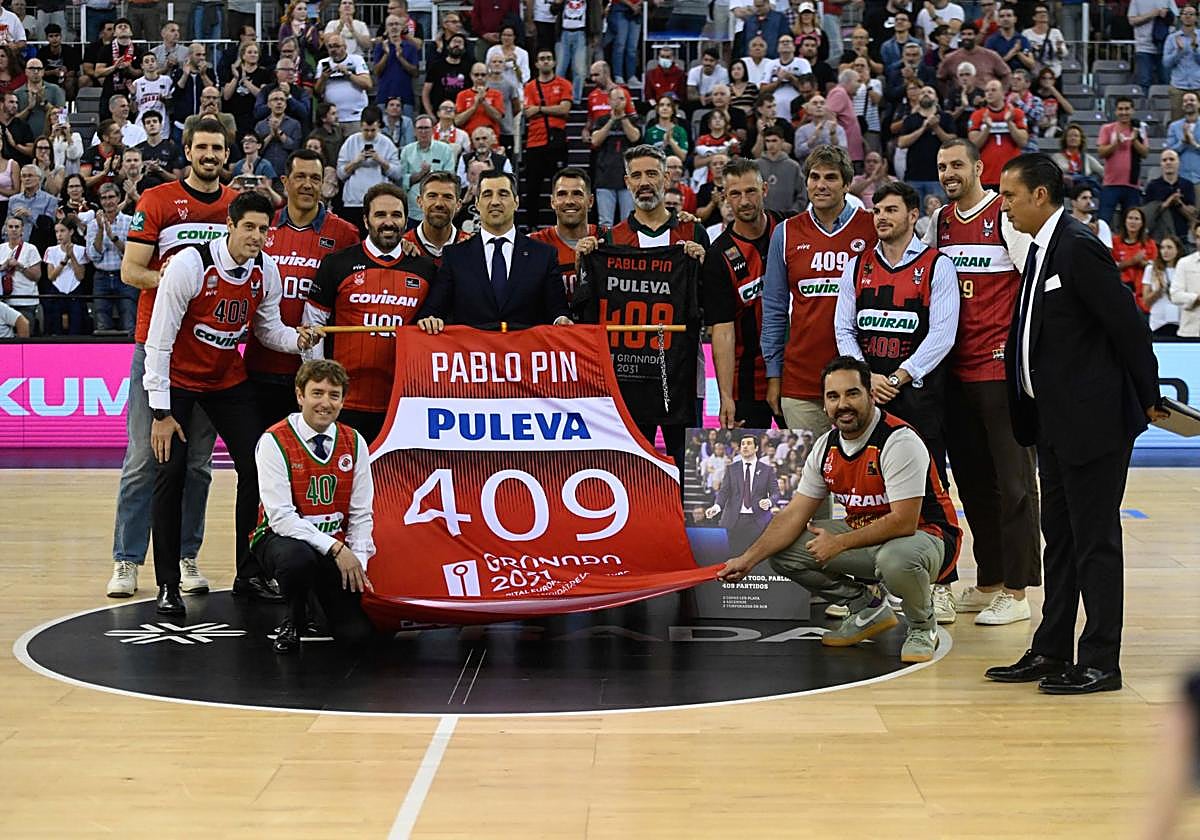 Pablo Pin, en el centro y con traje, sonríe durante su homenaje en el Palacio de Deportes junto a antiguos jugadores del club a los que entrenó como nazarí.