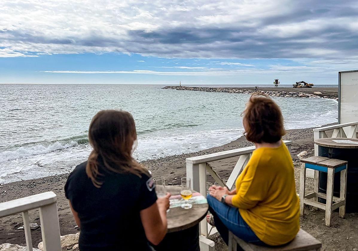 Unas vecinas observan en la terraza de un chiringuito, el espigón terminado.