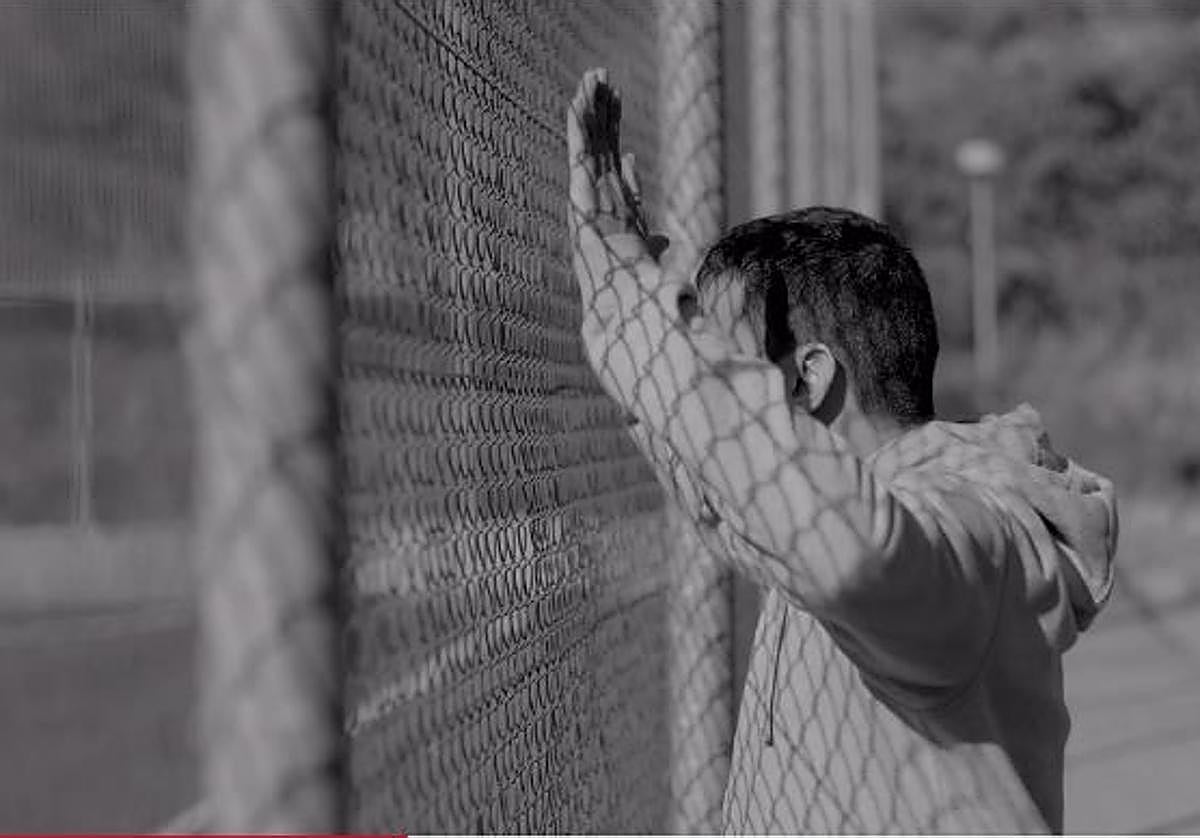 Un padre protesta, pegado a la valla, mientras su hijo juega.