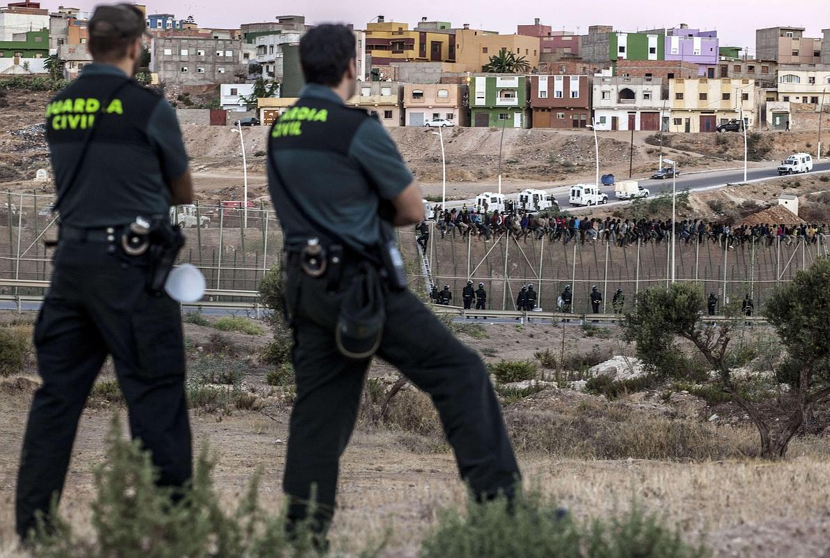 Miembros de la Guardia Civil vigilan a inmigrantes subsaharianos encaramados a la valla de Melilla. 