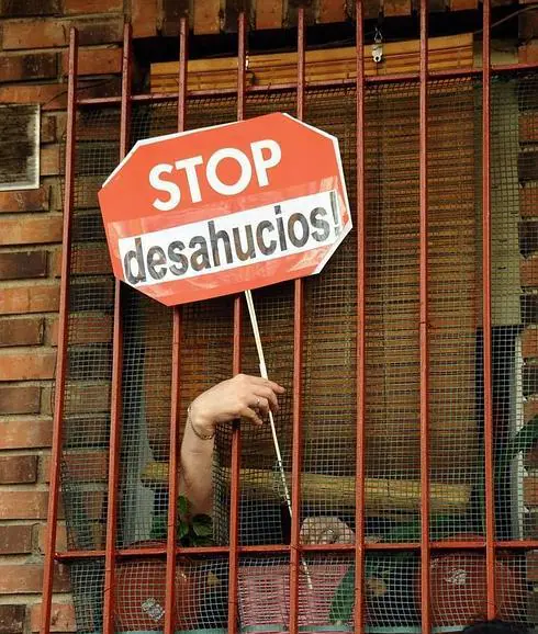 Una mujer cuelga un cartel de Stop Desahucios en su casa 