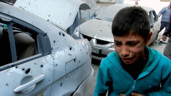Un niño sirio llora junto dos vehículos llenos de agujeros de bala.
