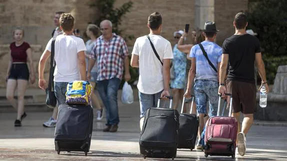 Cuatro jóvenes turistas caminan con su maletas por la plaza de la Virgen de Valencia. 