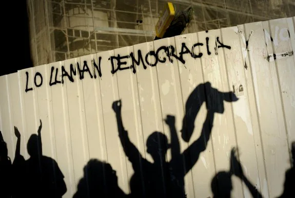 Las sombras de algunos jóvenes se reflejan en una valla en la que hay escrita una proclama de protesta, durante una concentración contra el desempleo juvenil en la UE.